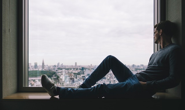 Image of a man leaning on the window overlooking a city.